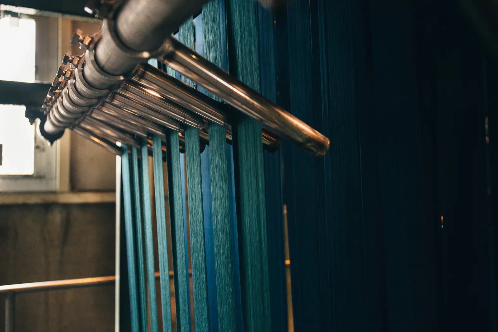 Sheets of indigo-dyed warp thread hanging from a copper roller at Kuroki Mills in Okayama, shading from pale teal to near-black — the denim behind the email programme that produced $541K in six months