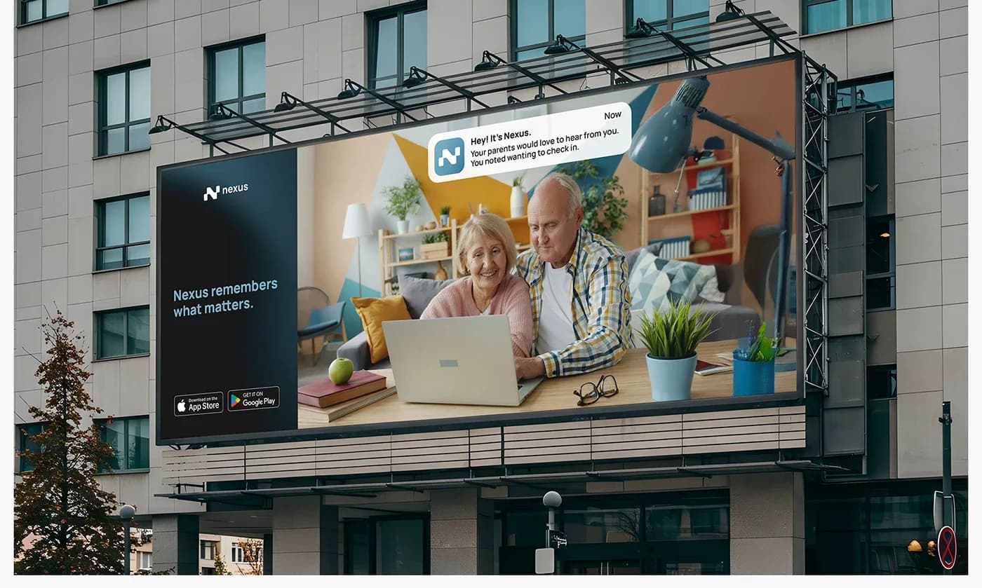 A large Nexus billboard mounted on an office building, showing an older couple at a laptop under a reminder to check in with their family