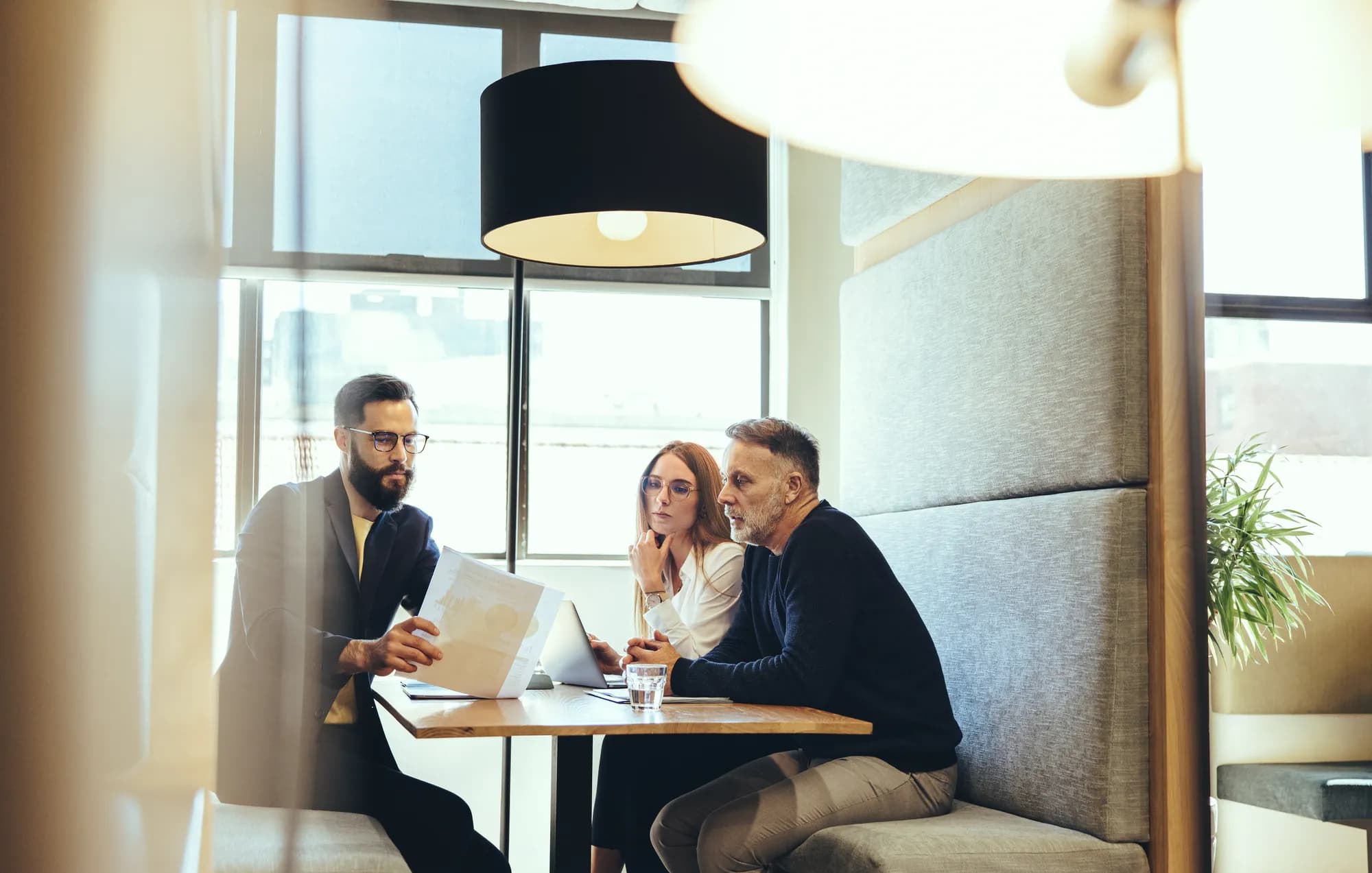 Three colleagues in a booth at a meeting table, reading a printed chart together