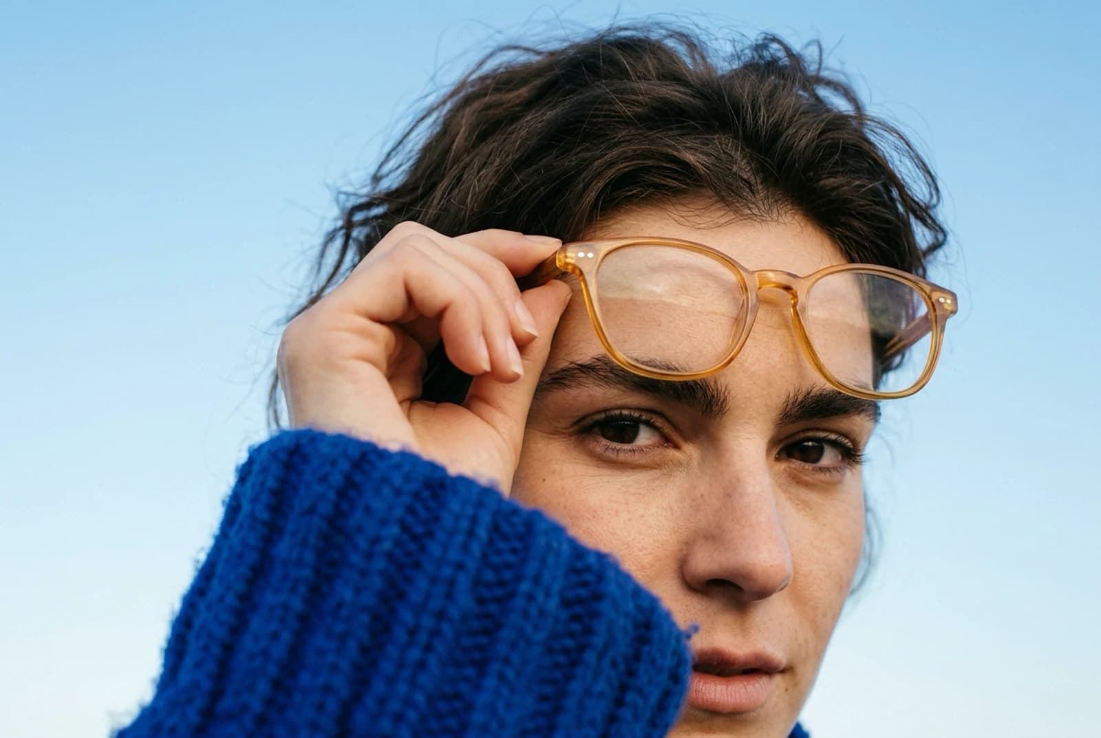 The source frame behind the first panel: a woman in a blue knit lifting her glasses, lit high and cool