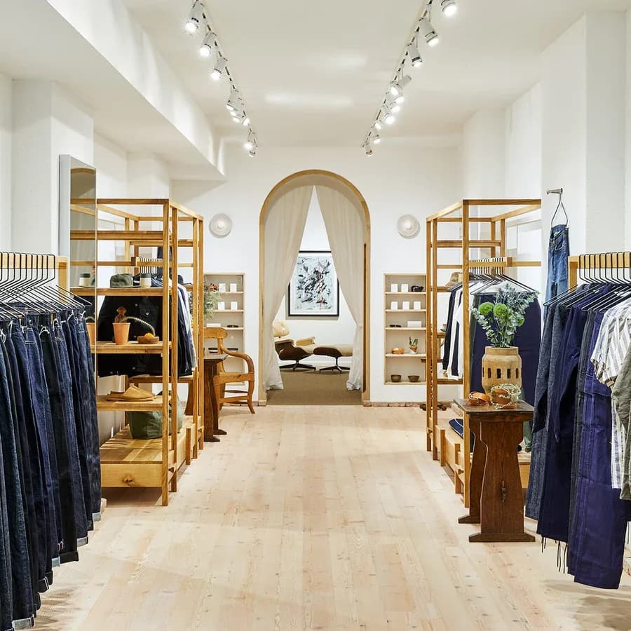 The 3sixteen shop interior: rails of indigo denim on oak fixtures under track lighting, a curtained archway at the far end