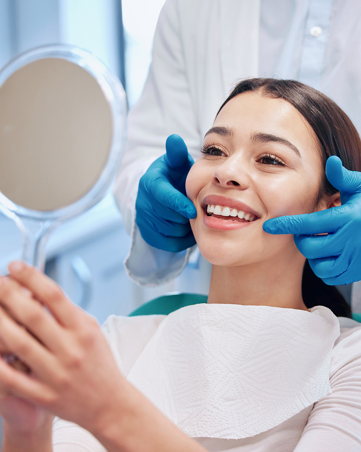 A patient holding a hand mirror while her dentist checks her smile.