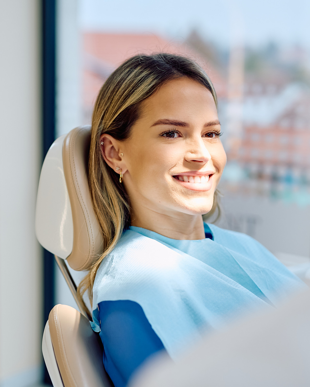 A smiling patient sitting in the chair beside a bright window.