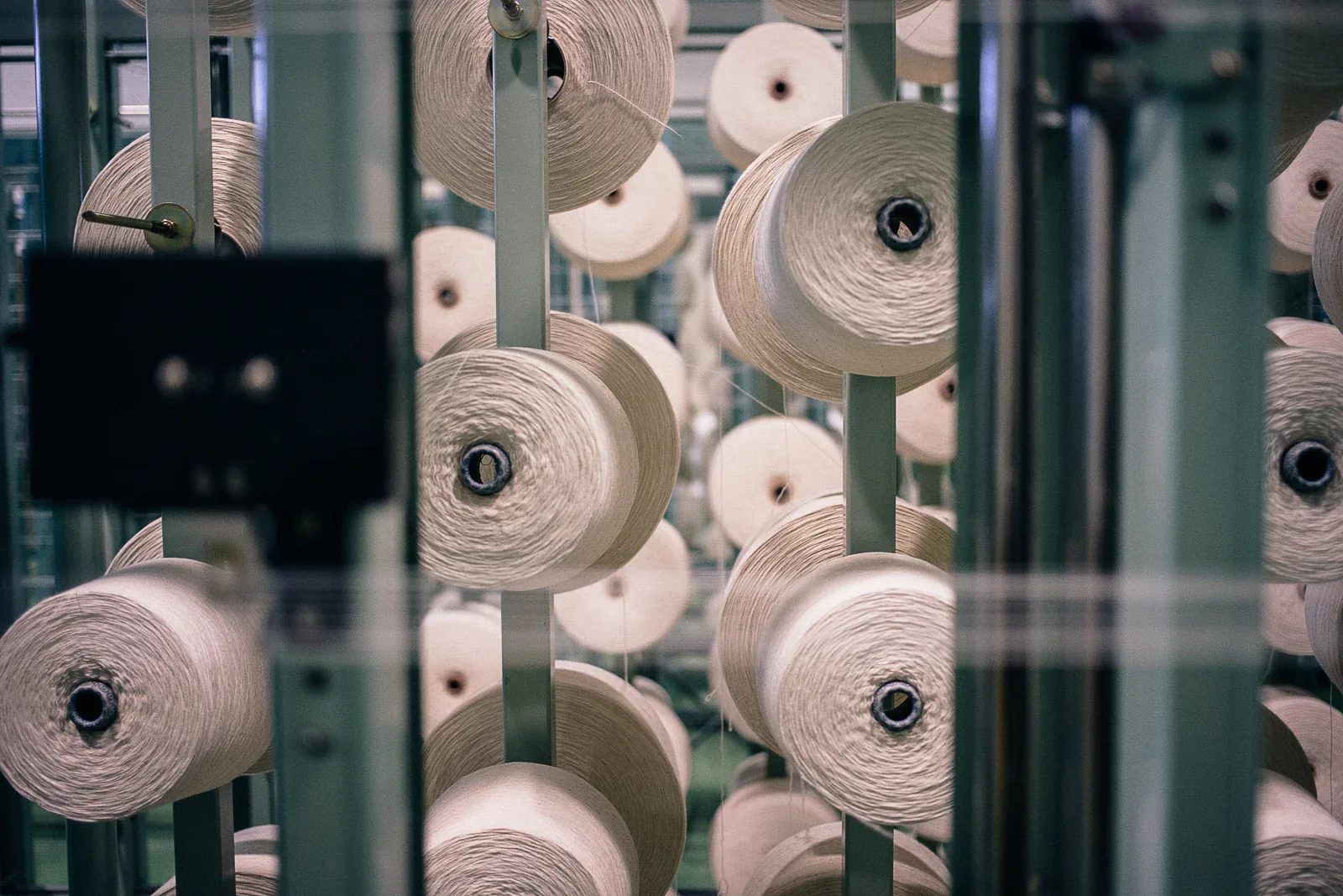 Cones of undyed cotton yarn stacked on a warping creel behind glass at Kuroki Mills