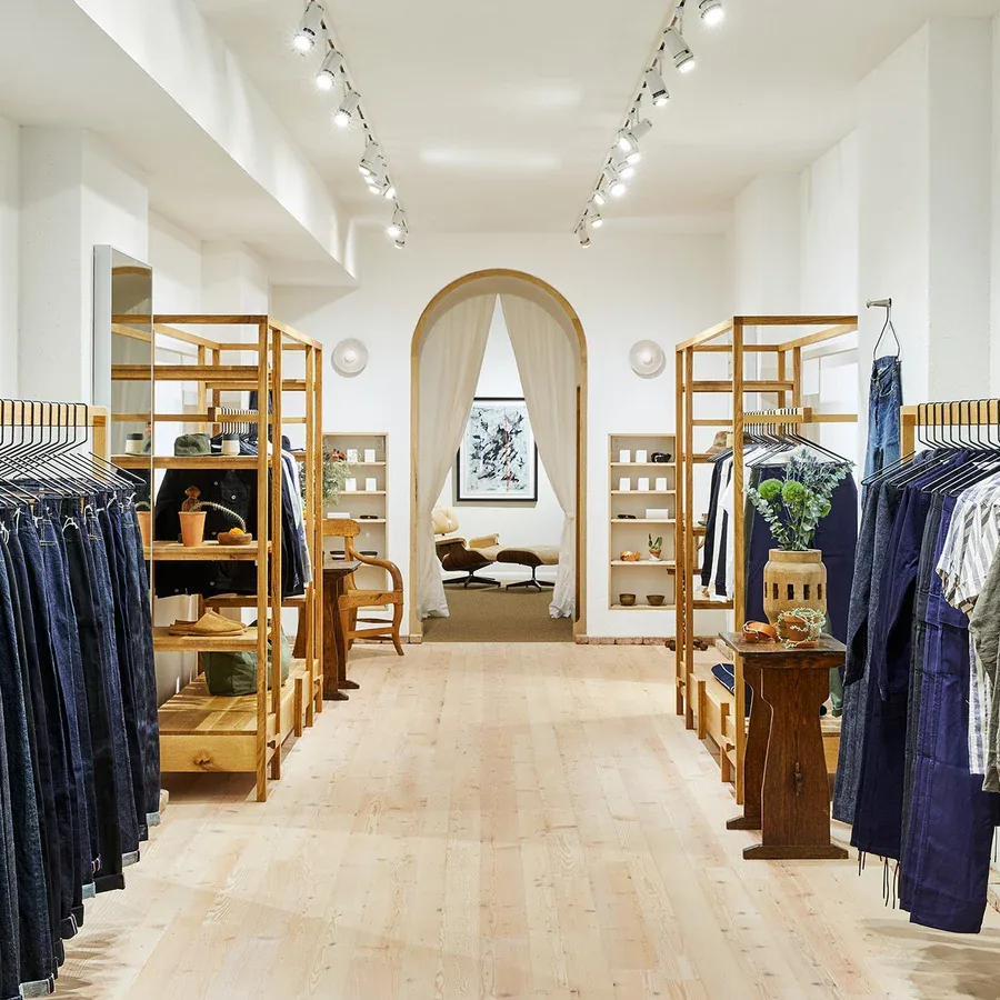 The 3sixteen shop interior: rails of indigo denim on oak fixtures under track lighting, a curtained archway at the far end