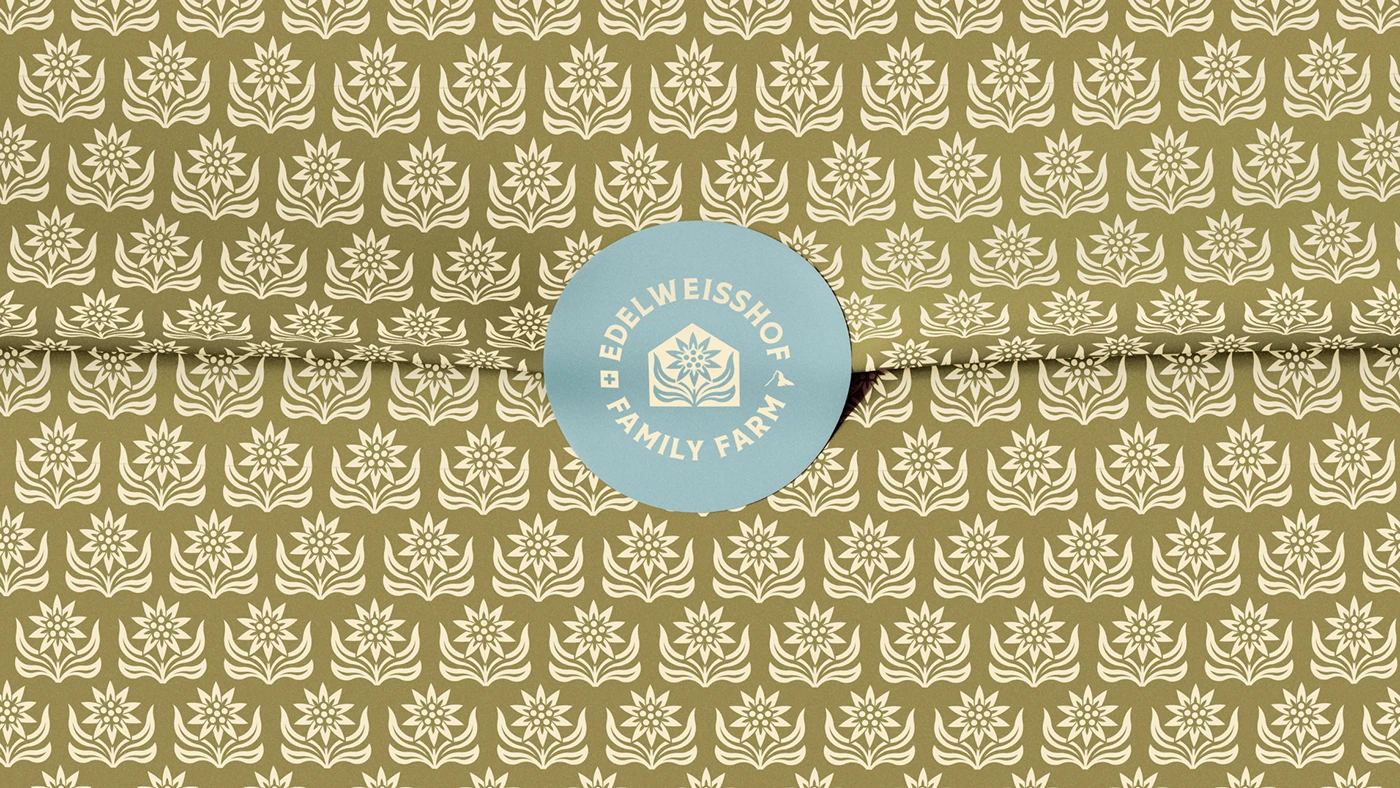 The Edelweisshof block-print pattern in bone on moss green wrapping paper, closed with a pale blue circular seal carrying the crest