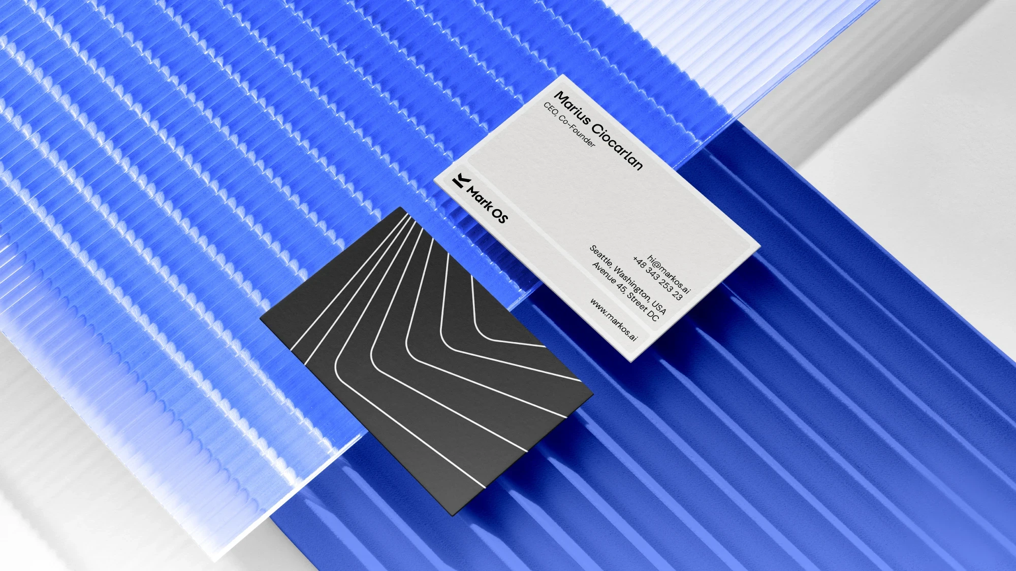 Two Mark OS business cards resting on ridged blue acrylic — a pale front and a black patterned reverse