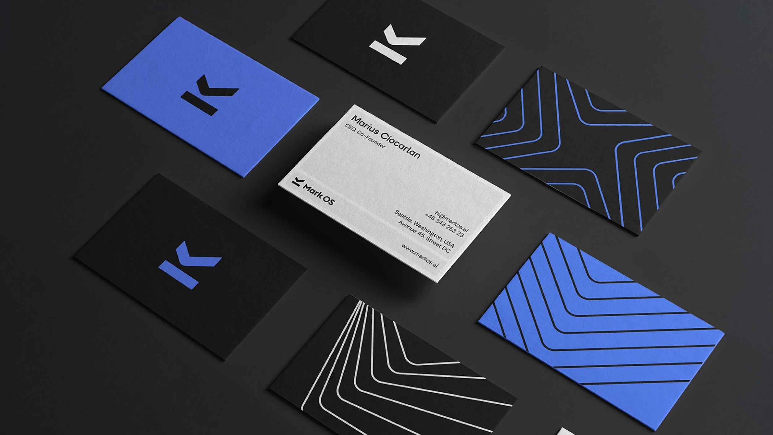 The Mark OS stationery suite on black: business cards in blue, black and white, patterned reverses, and the founder's card in embossed stock