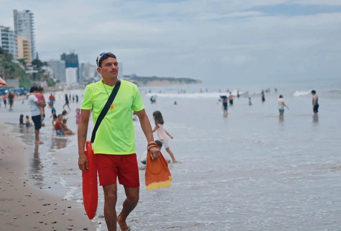 A lifeguard walking the shoreline at Manta carrying a rescue can and fins