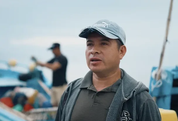 Henry Dávila, a fisherman, speaking to camera on the deck of a blue fishing boat in Manta