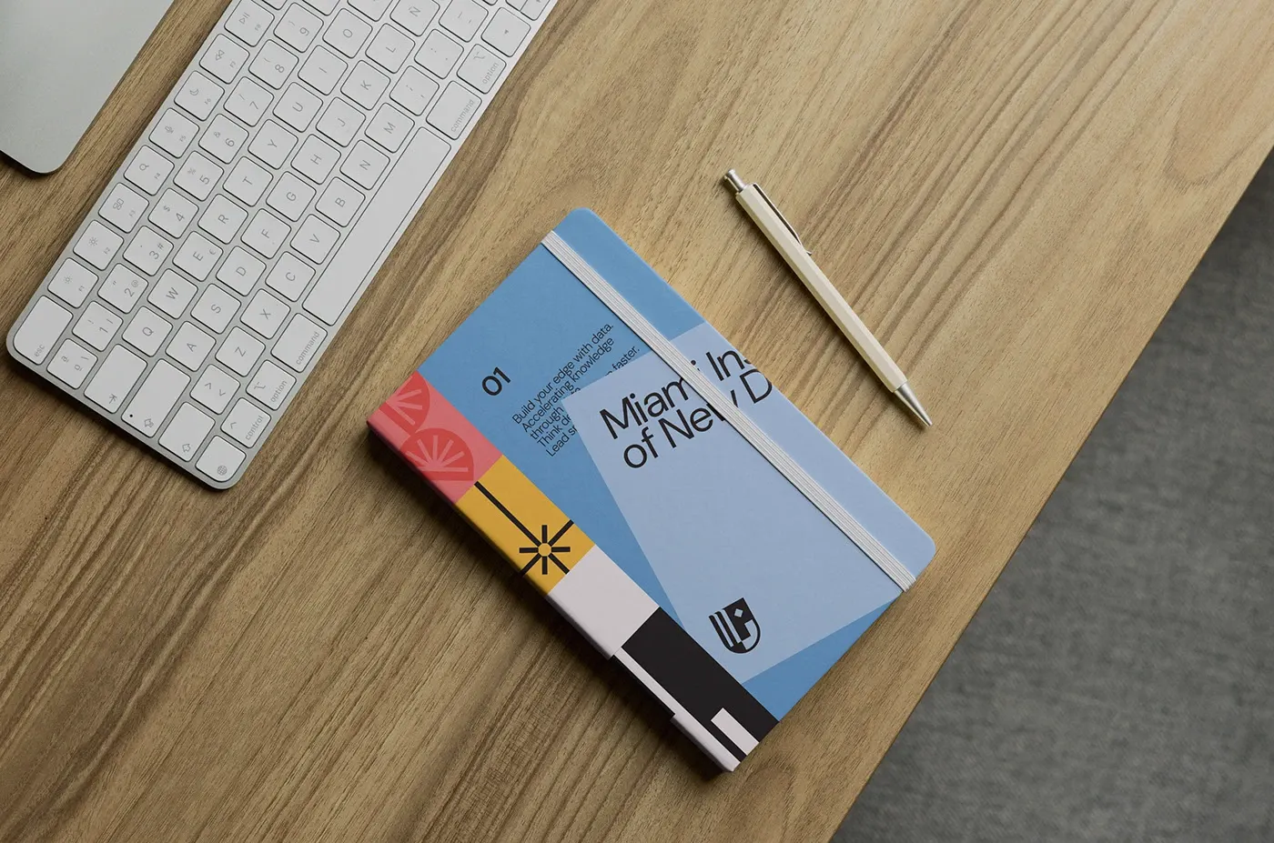 A pale-blue programme notebook with a colour-blocked spine on a walnut desk.