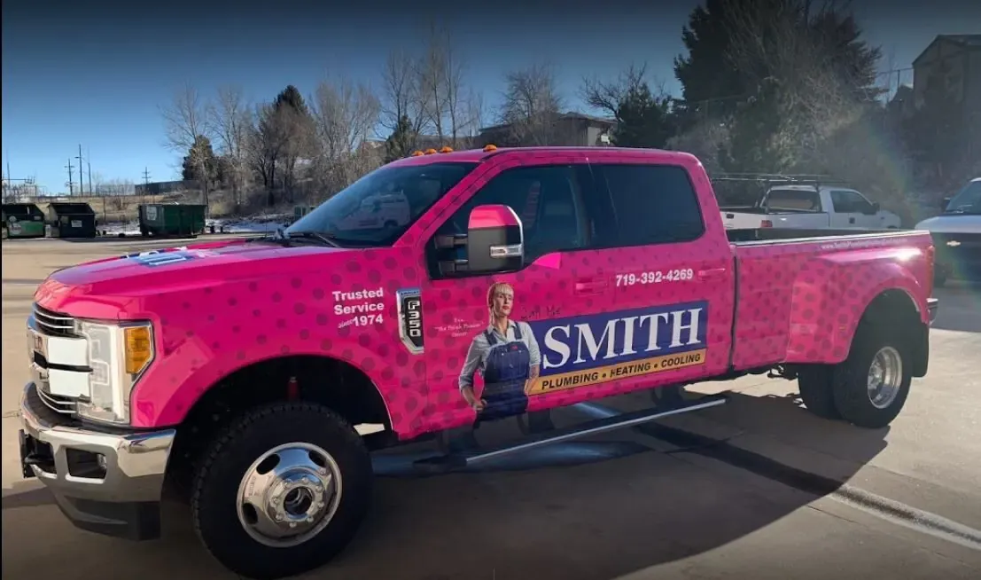 Pink Smith pickup with a navy Smith Plumbing Heating Cooling panel and a woman in overalls illustrated on the door