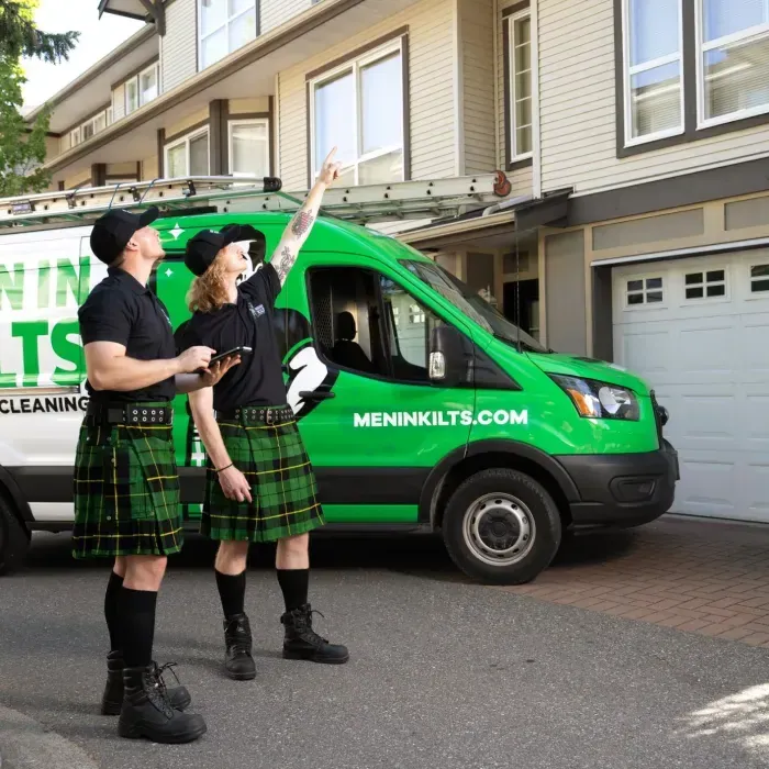 Two Men In Kilts technicians in green tartan kilts and black shirts beside a green branded van in a driveway