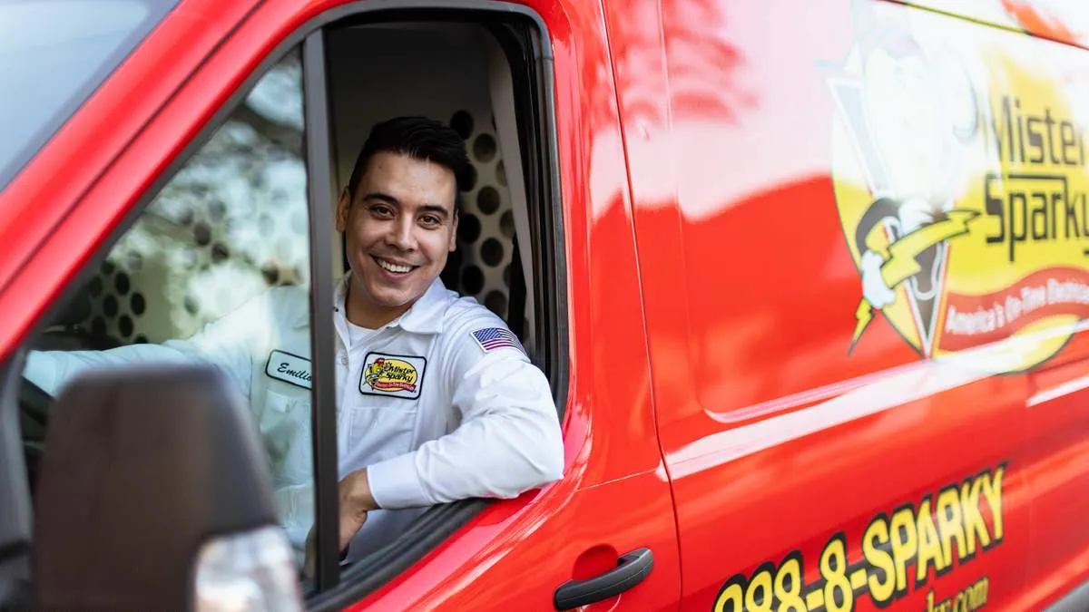Smiling Mister Sparky electrician leaning from a red van, with the cartoon mascot and on-time tagline on the side panel