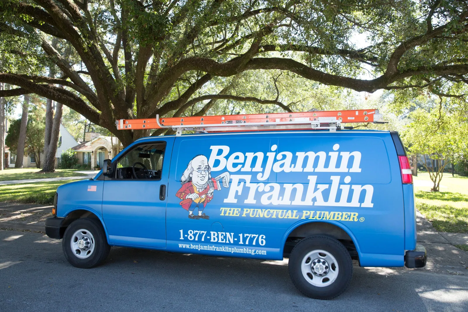 Blue Benjamin Franklin Plumbing van with a cartoon Ben Franklin and the words The Punctual Plumber on the side