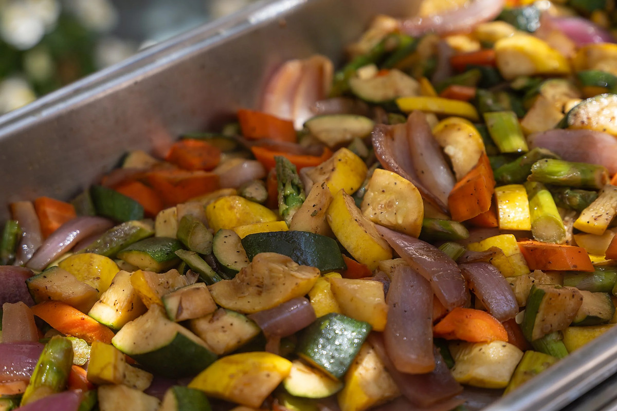 A deep tray of roasted vegetables straight off the heat: courgette, red onion, yellow squash, carrot and peppers.
